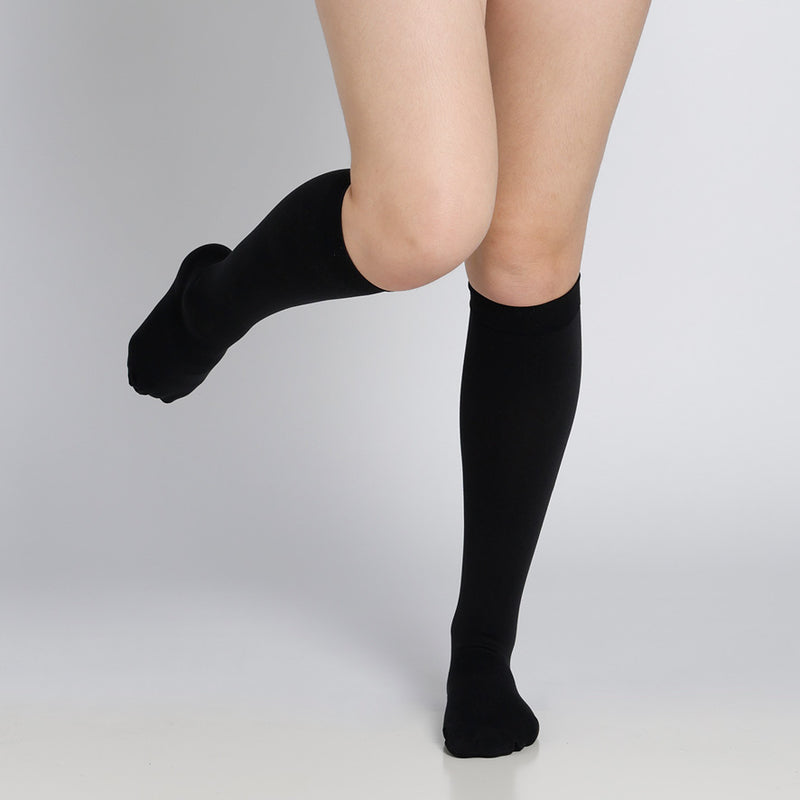 Black knee-high socks worn by a person on a light gray background