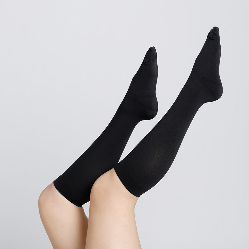 Black knee-high socks worn by a person on a light gray background